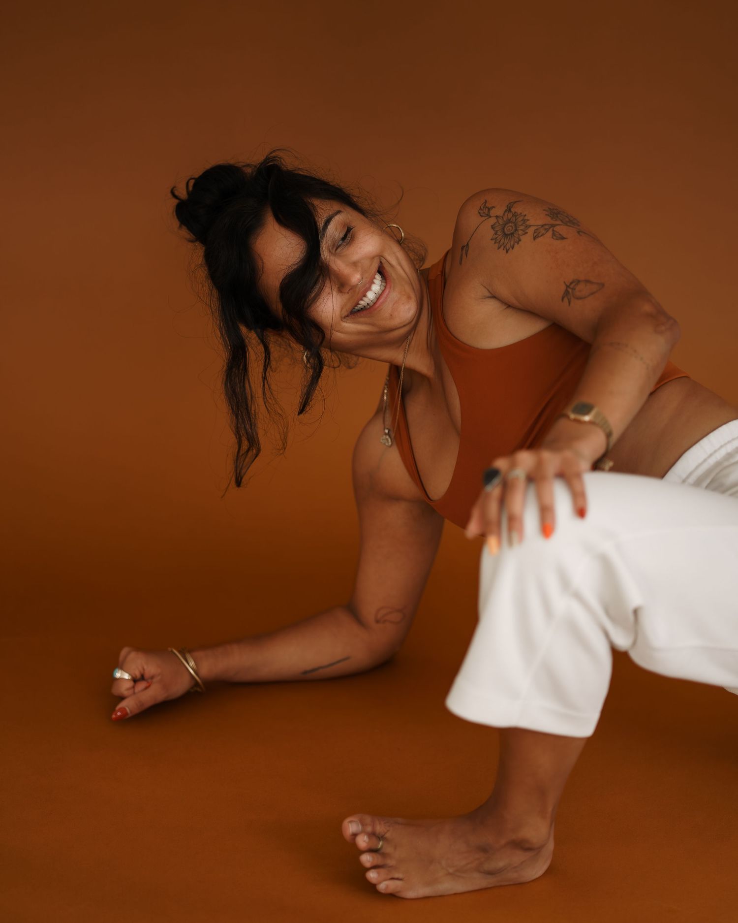 Athletic figure in rust-colored top and white pants stretches on a brown studio backdrop.