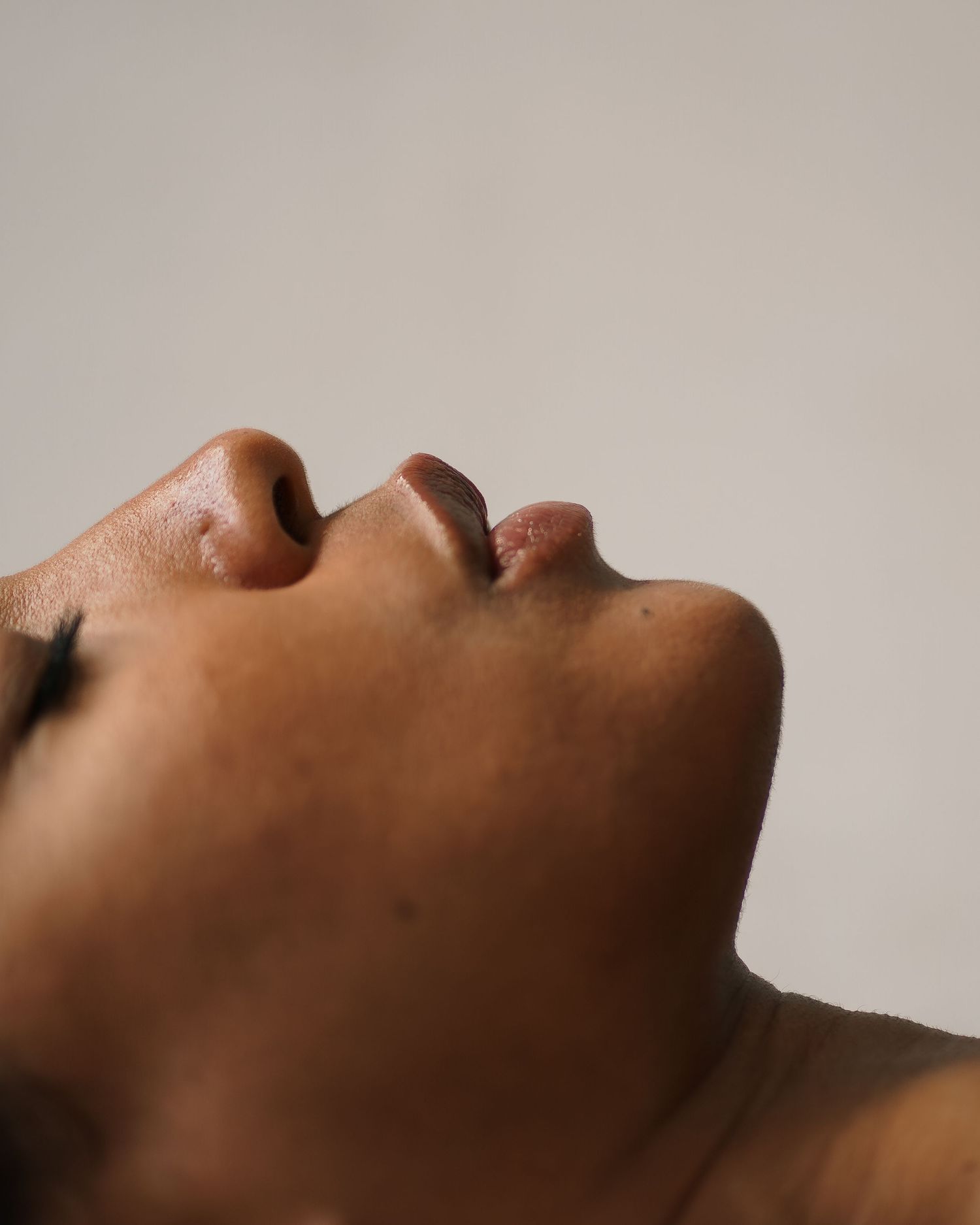 Close up profile of skin with water droplets against neutral background.