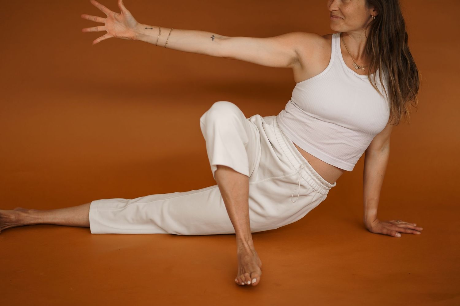 Woman in white athletic wear performing a stretching pose on brown background during yoga or pilates session.