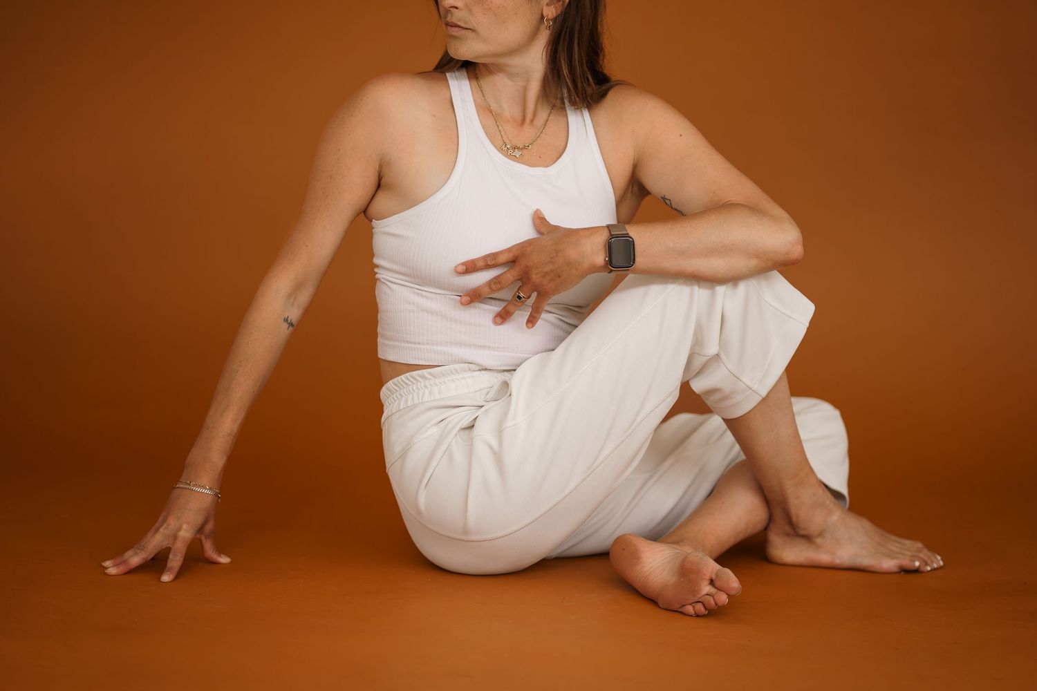 Minimalist pose of someone in white athletic wear seated on burnt orange floor.
