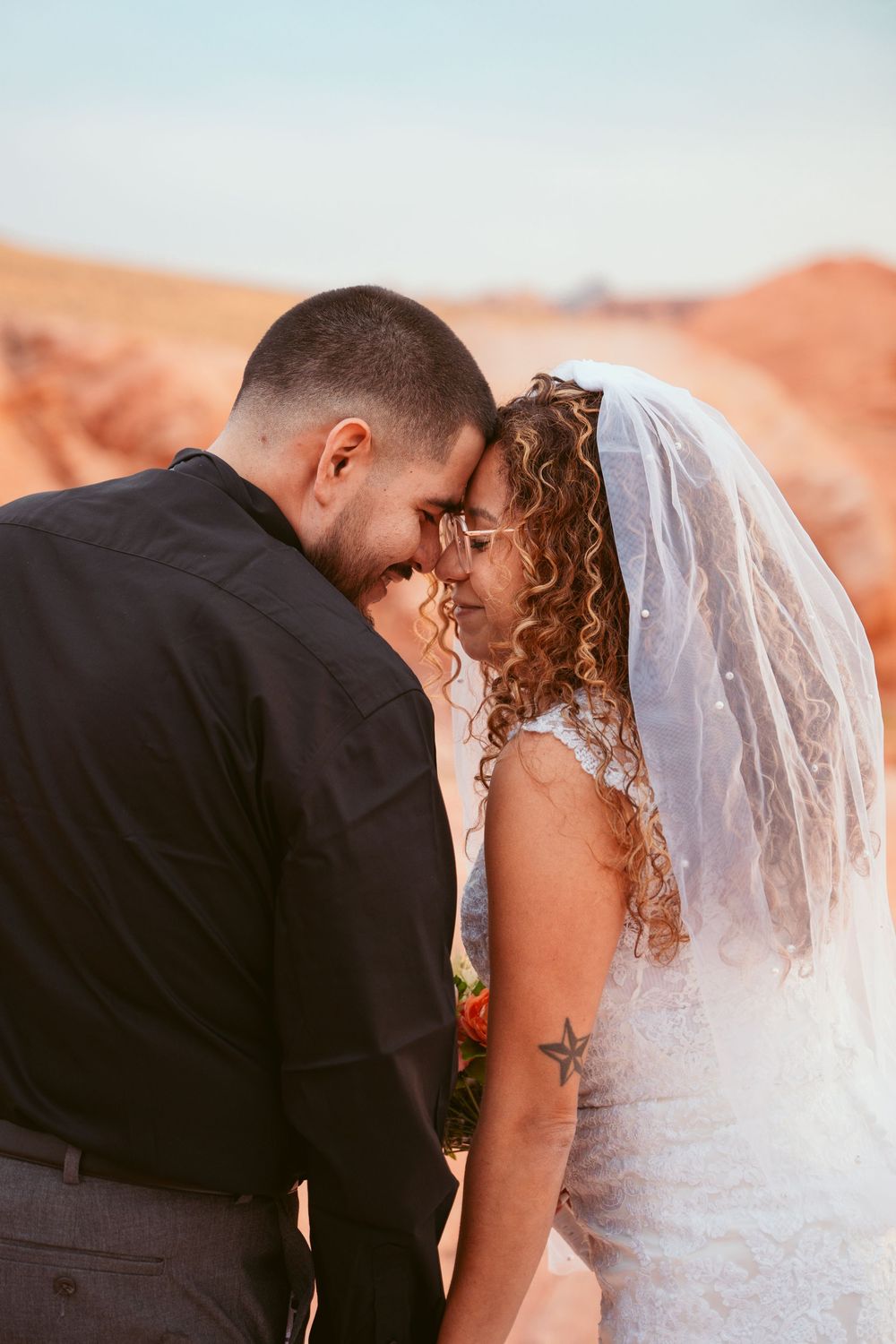 A romantic wedding couple share intimate moments against a stunning desert backdrop at sunset.