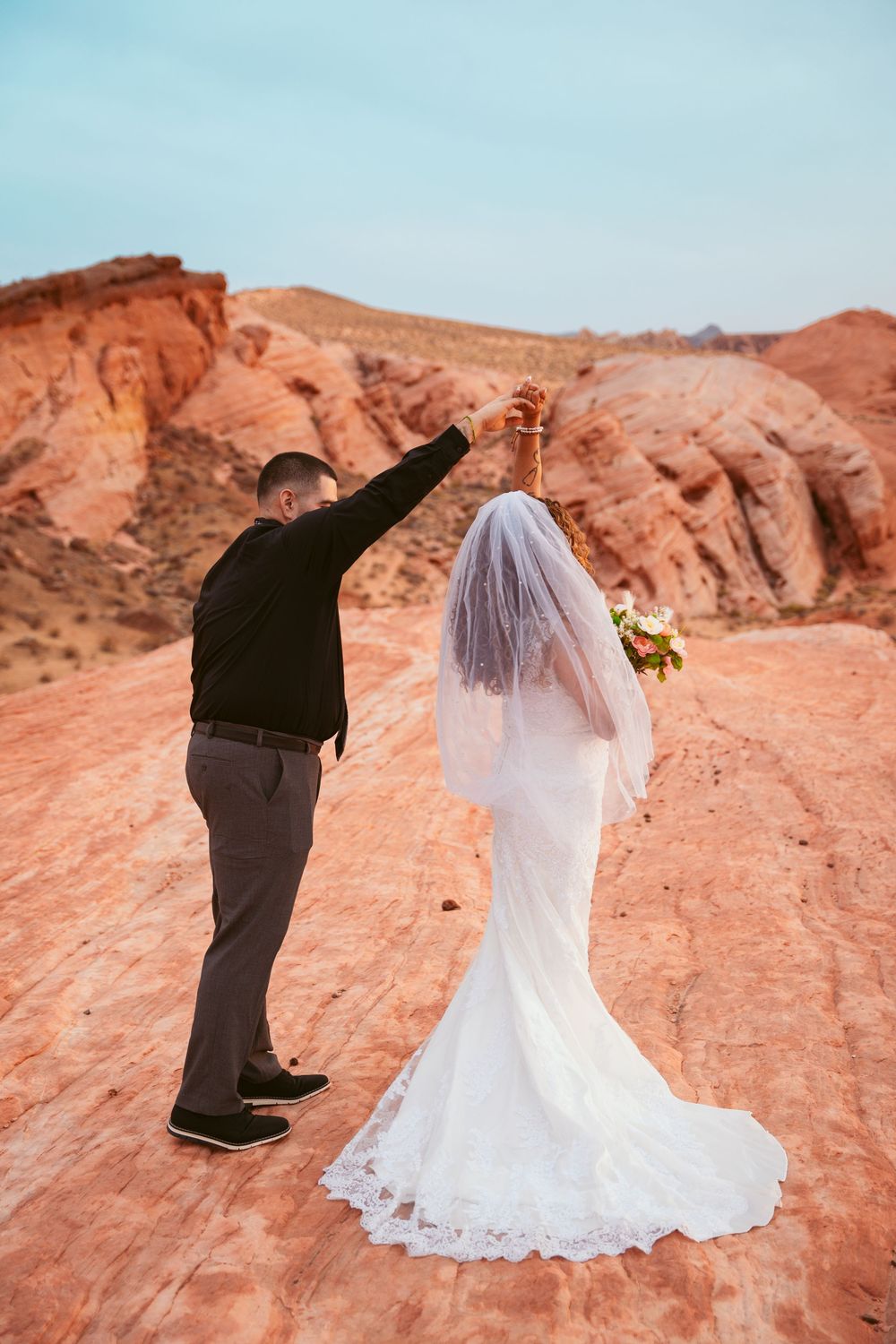 A wedding couple poses against dramatic red rock formations in the desert at sunset creating silhouette photos.
