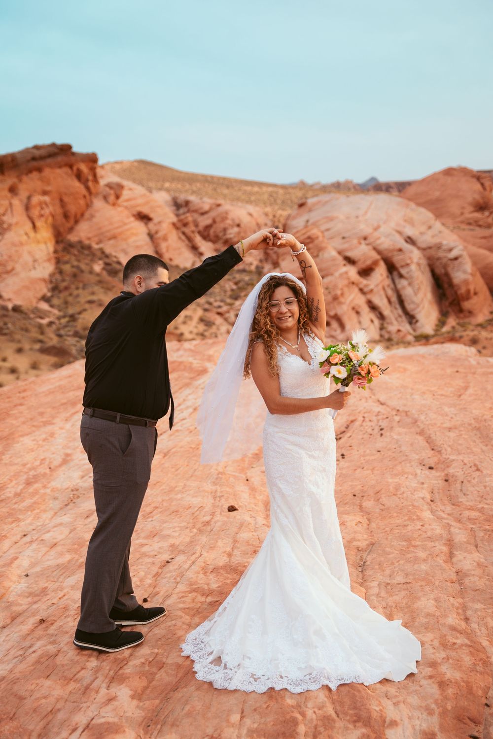 Wedding photoshoot on red rock formations with couple in traditional attire walking along natural formations.