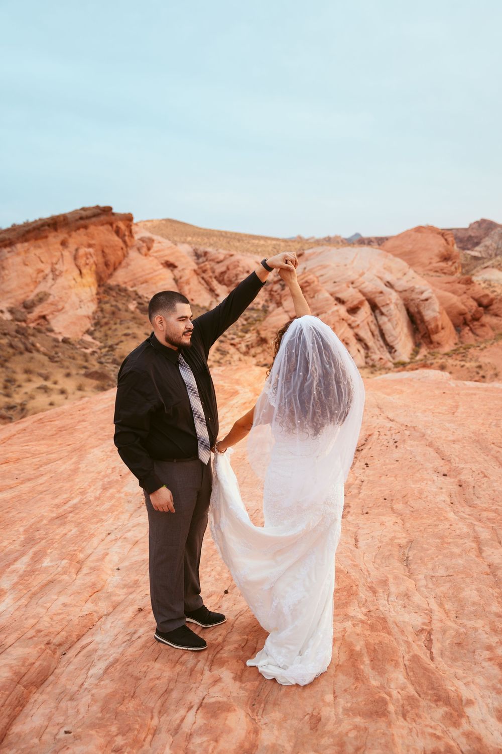 Wedding couple shares an intimate moment while dancing on red rock formations in the desert.