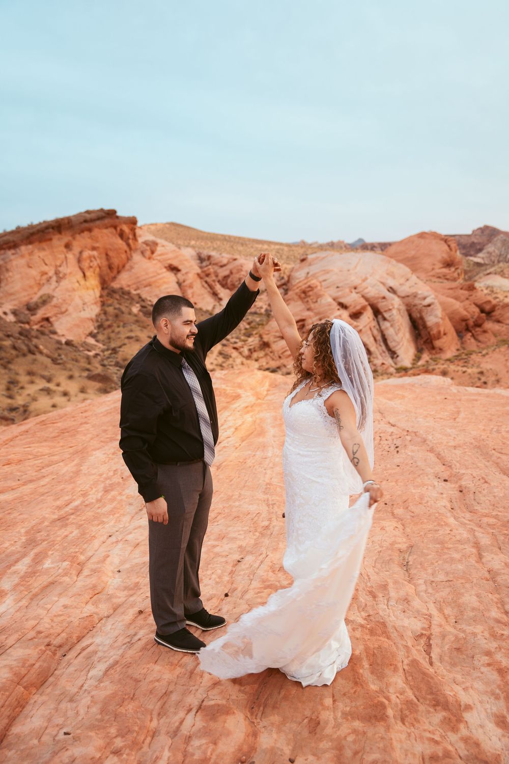 Newlyweds share a playful dance together on scenic red rock formations at sunset.