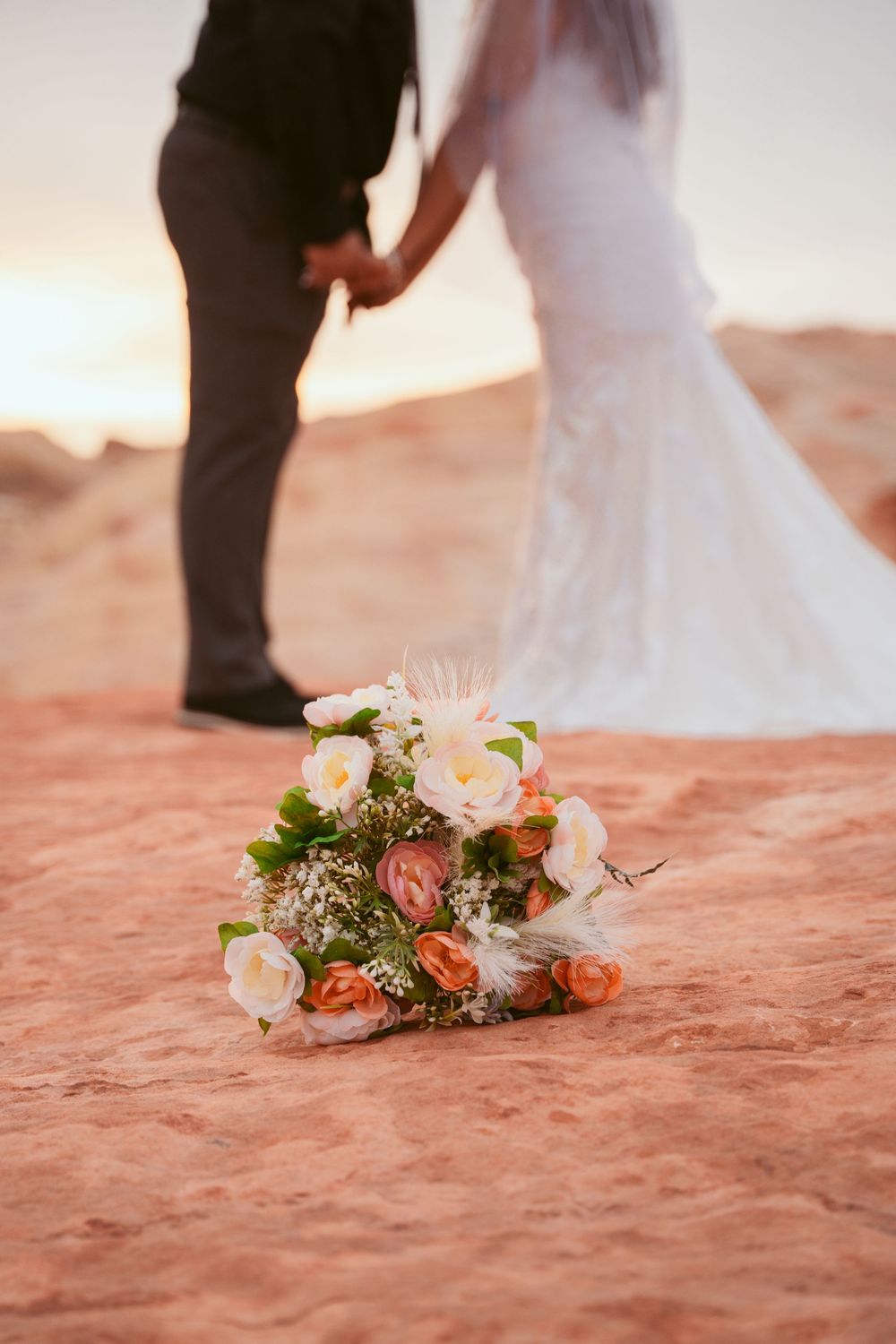 A bridal bouquet with pink and white flowers lies on red desert rock during sunset.