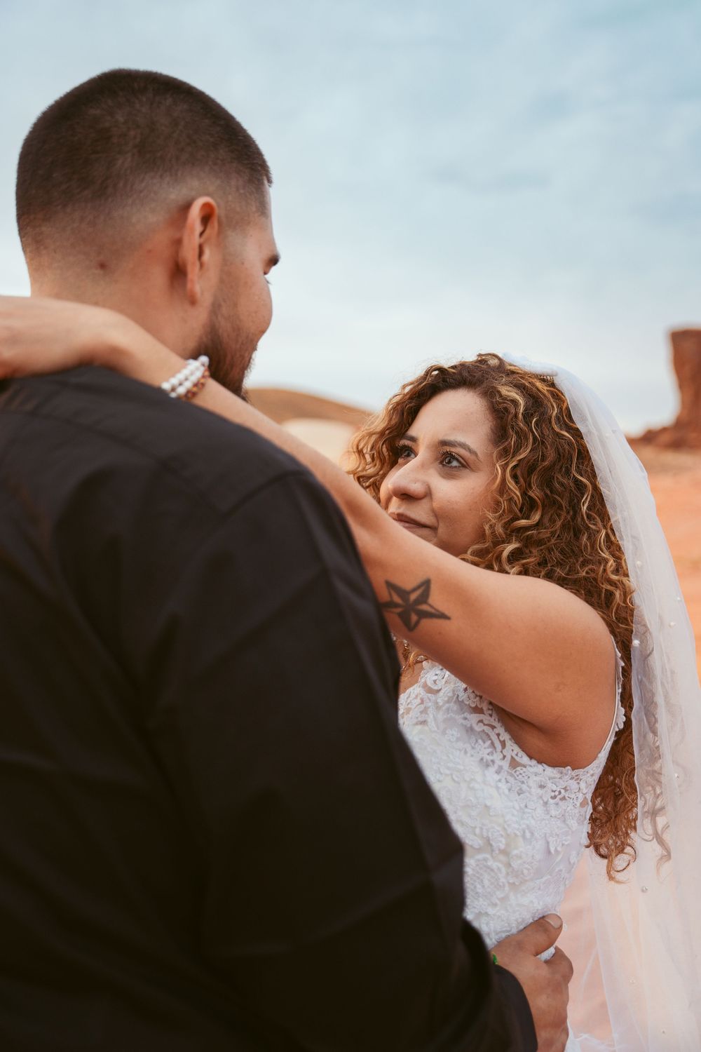 Intimate wedding moment captured against desert rock formations and blue sky.
