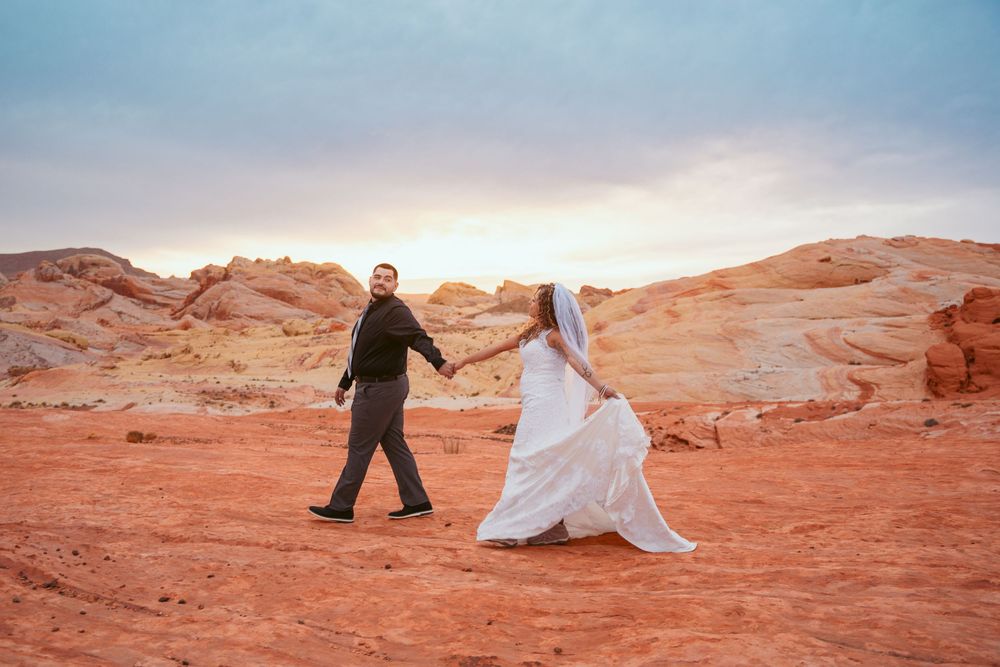 Wedding couple walking through scenic red rock desert landscape at sunset.