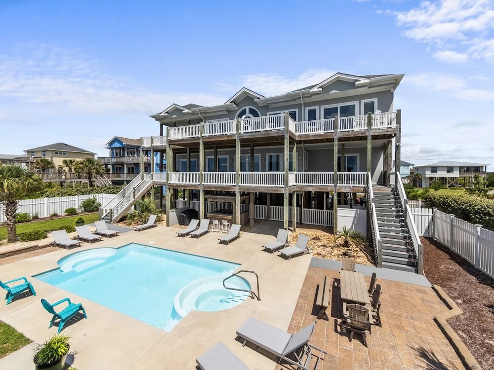 Large oceanfront vacation homes with pools and decks line the beachfront under sunny blue skies.