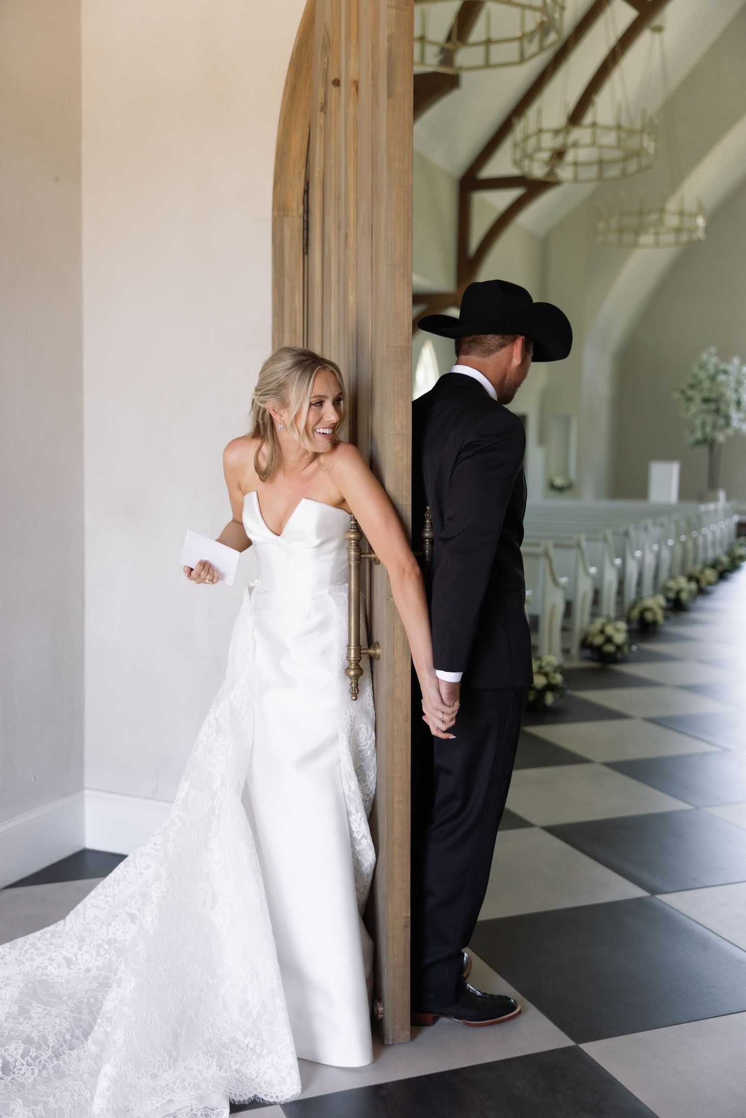 Bride and groom share a playful first look moment on opposite sides of a doorway in a church hallway.