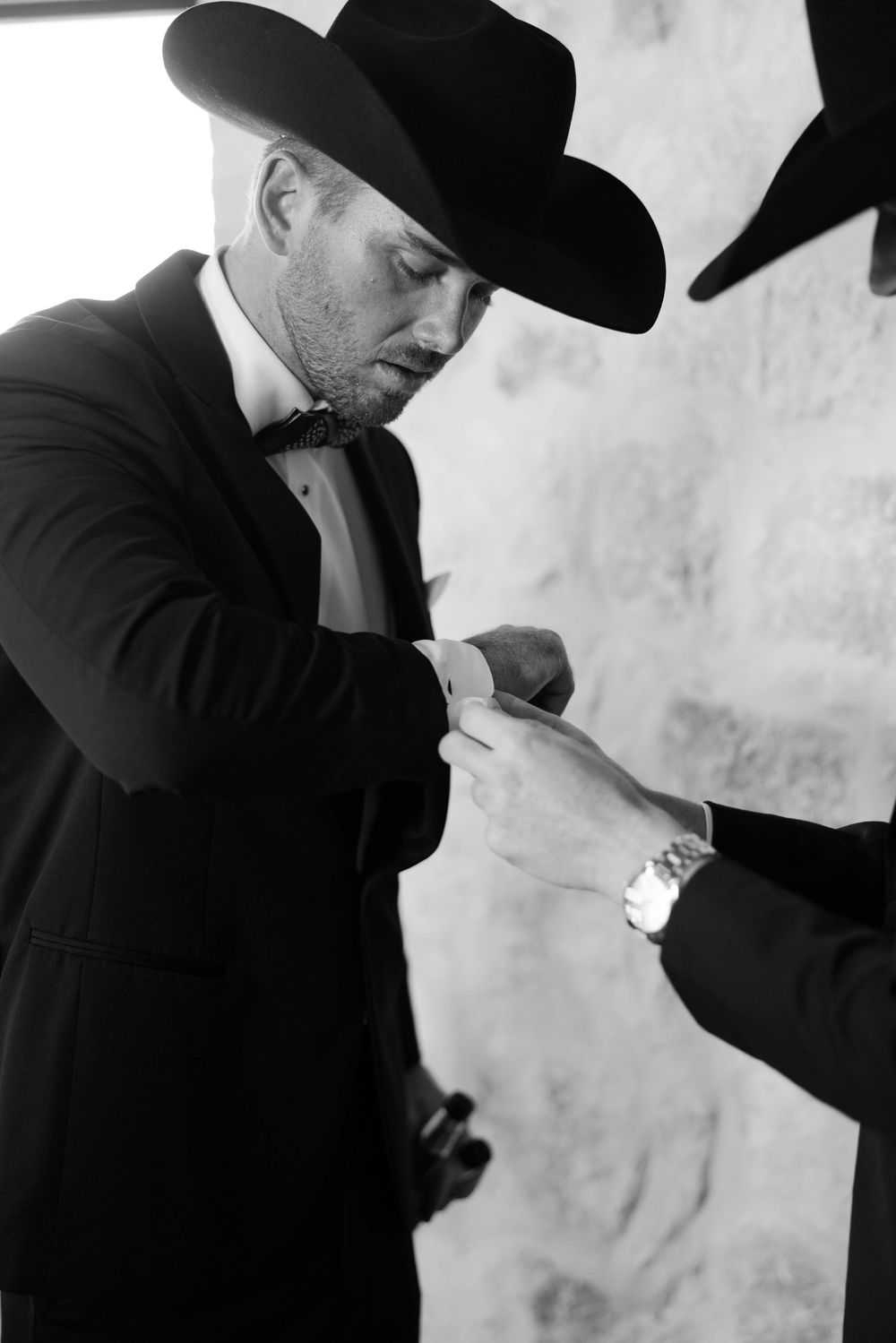 Black and white photo of groomsman adjusting cuffs while wearing western formal attire.