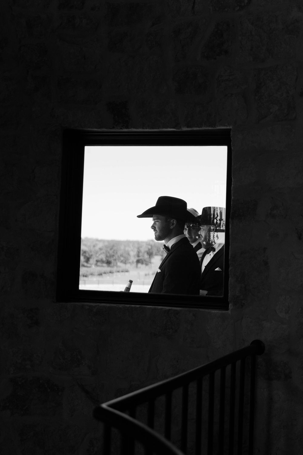 A black and white photograph showing figures in formal attire viewed through a square window frame.