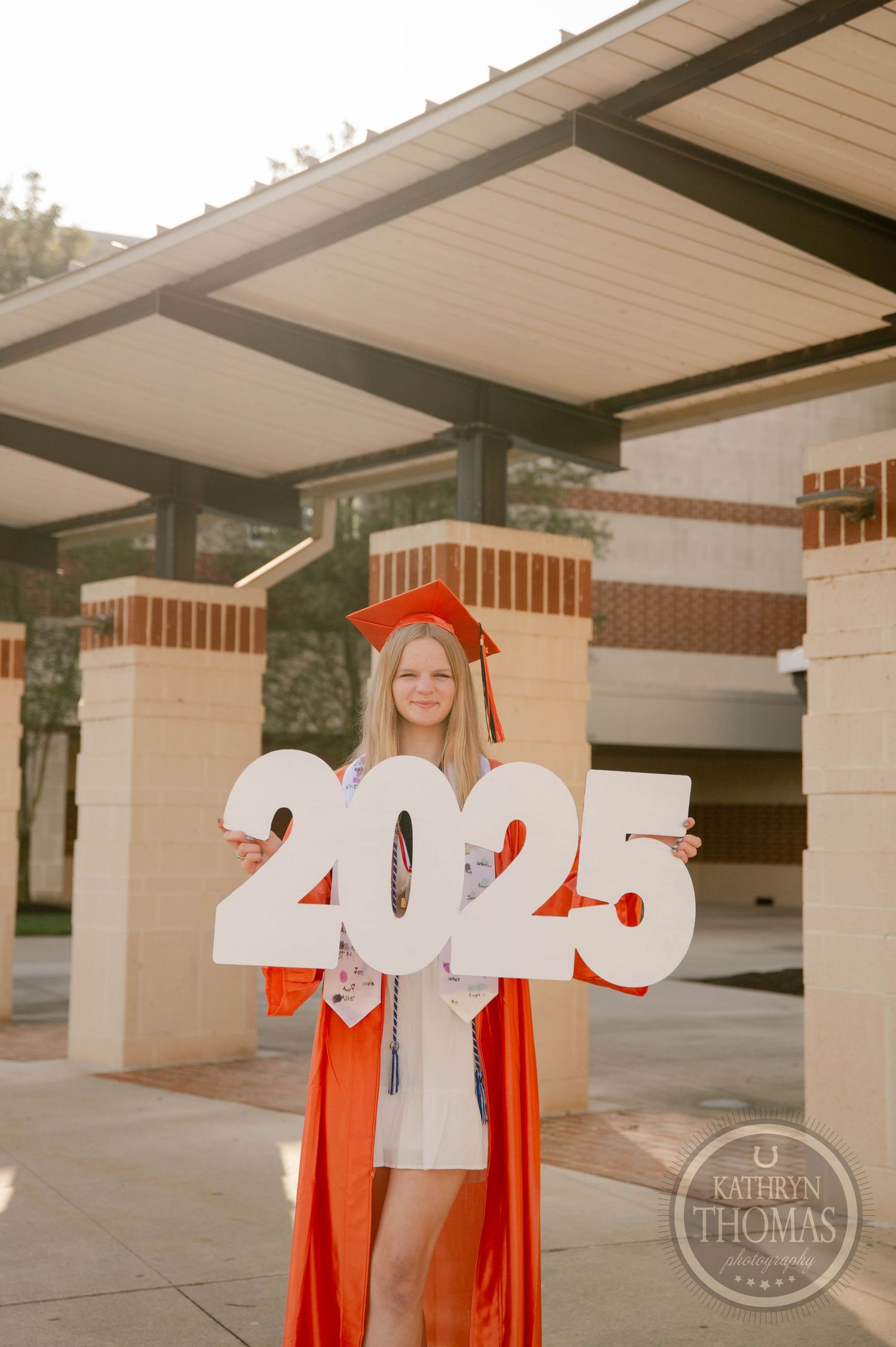 A graduate in red gown and gold cap poses with glowing numbers in a creative photo series against a modern building exterior.