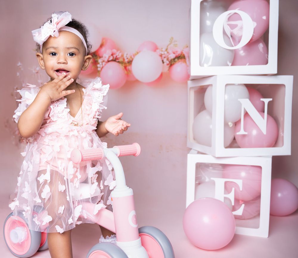 Pink birthday setup with decorative ONE boxes, balloons and floral garland in studio setting.