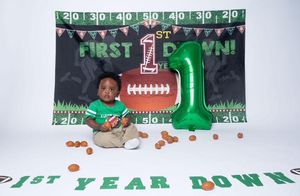 Football themed first birthday party setup with green number 1 balloon and yard line backdrop.