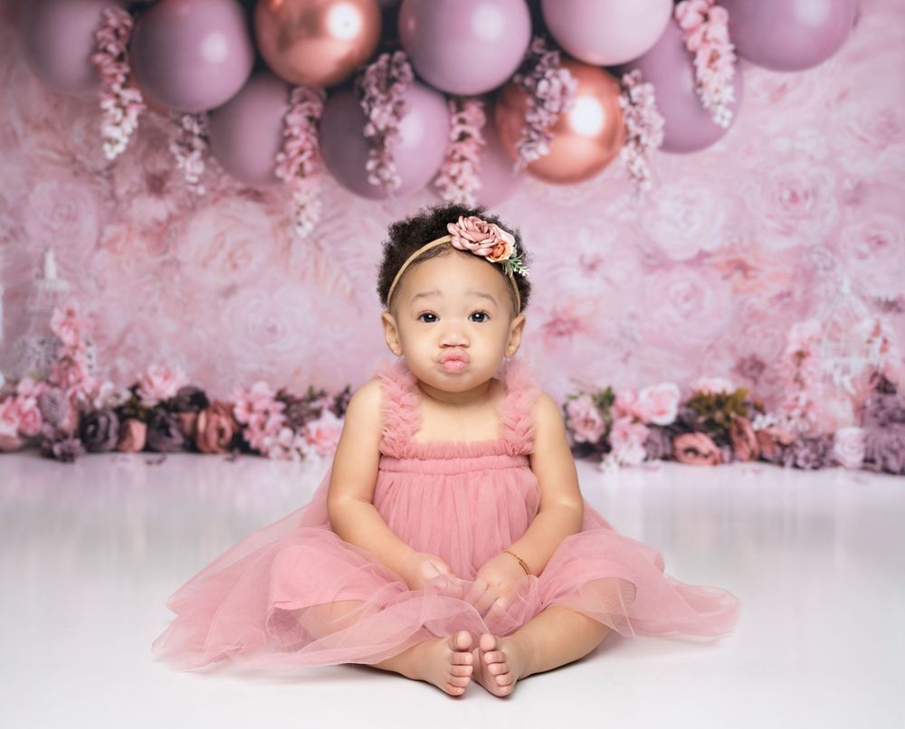 Pink and rose gold cake smash photo session setup with balloons and floral decorations against a textured backdrop.