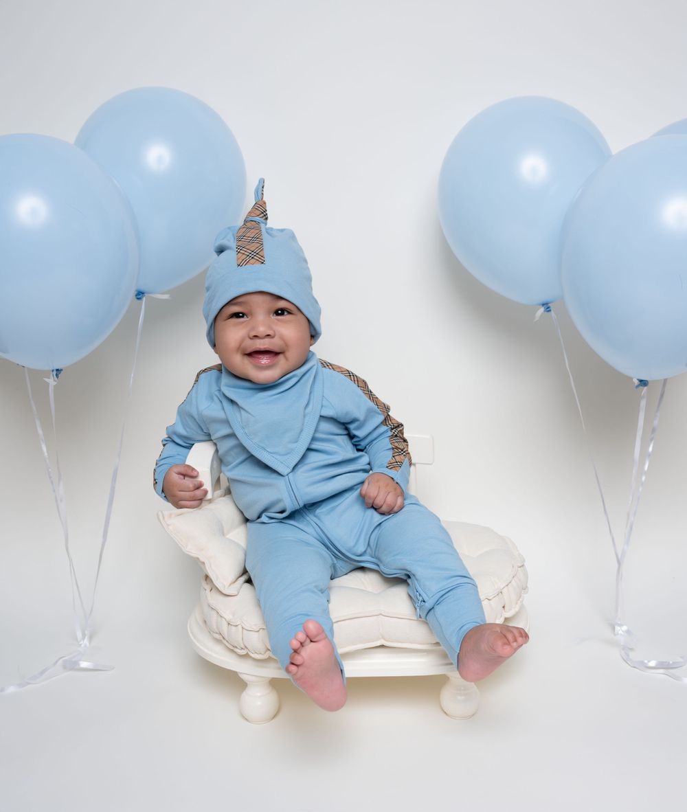 Smiling baby wearing blue gucci outfit seated with festive balloons.