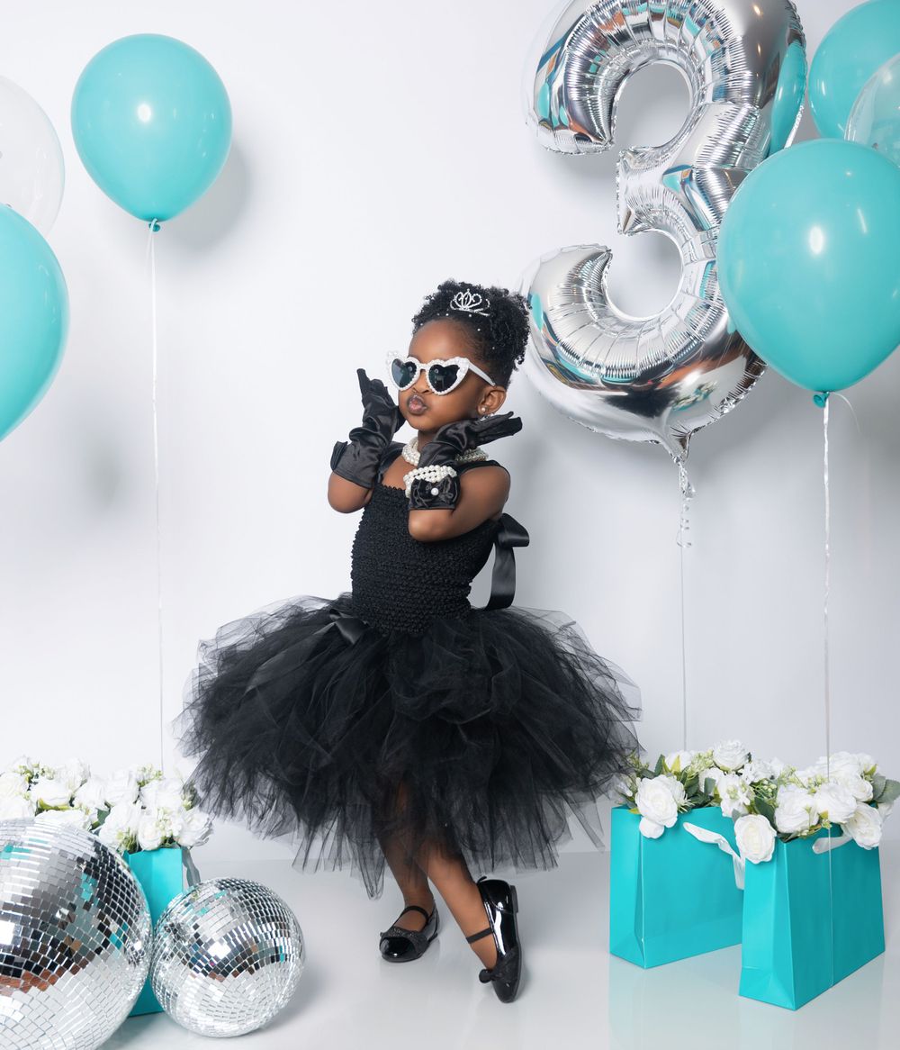 Party scene with tulle dress, disco balls, turquoise gift boxes and silver number 3 balloon against white wall.