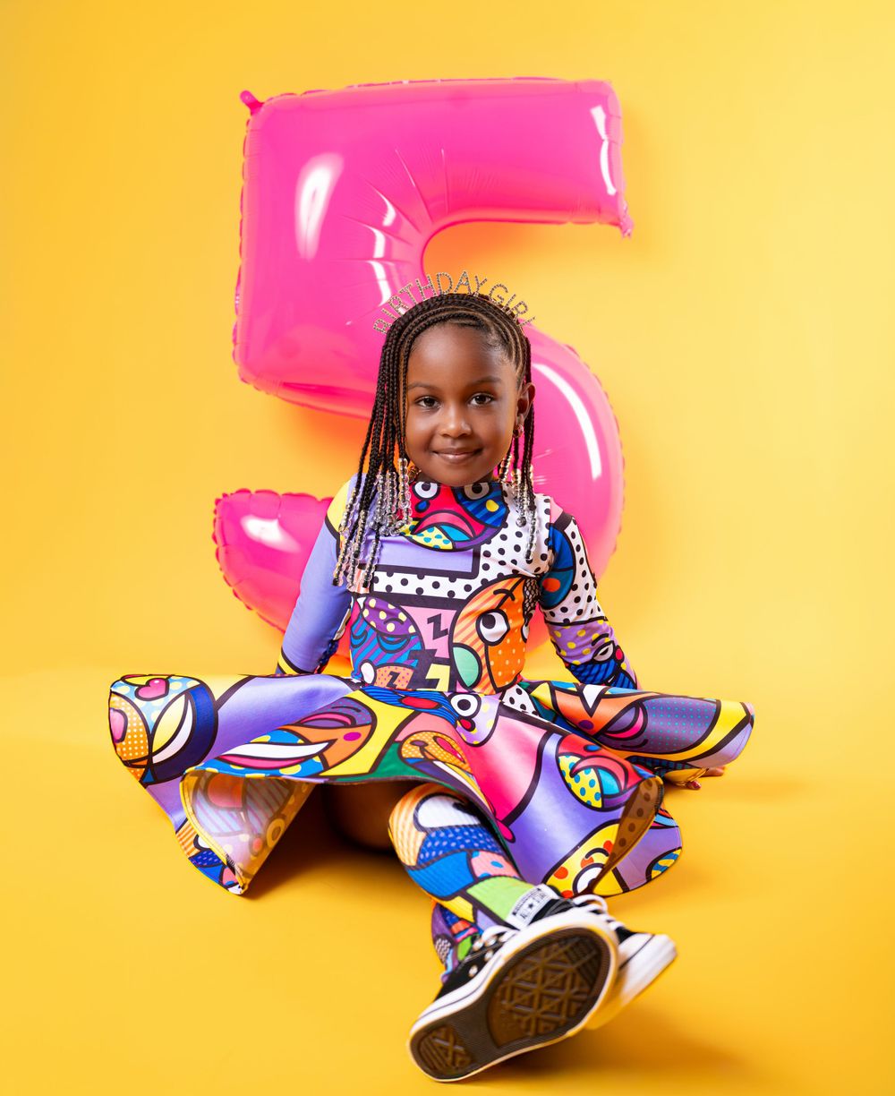 Vibrant patterned dress with pink number 5 balloon on yellow backdrop for milestone birthday photoshoot.