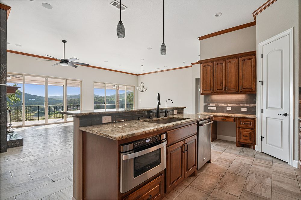 Modern kitchen with granite island, stainless appliances, and panoramic mountain views through large windows.