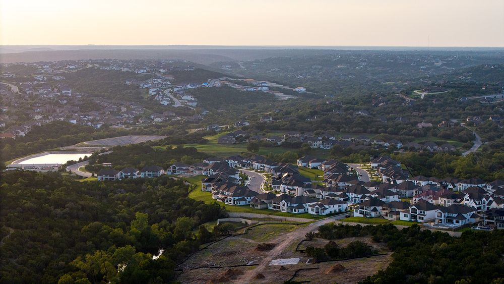 Aerial view of a coastal residential neighborhood with houses and a reflective lake at sunset.
