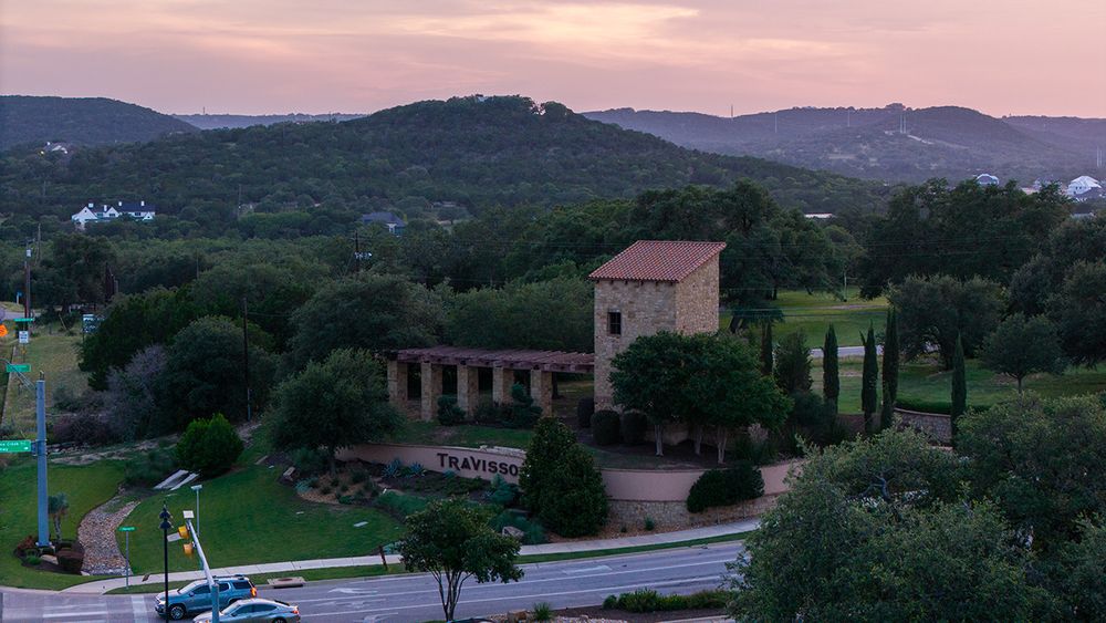 A stone building nestled in Texas Hill Country with rolling hills and a pink sunset sky in the background.