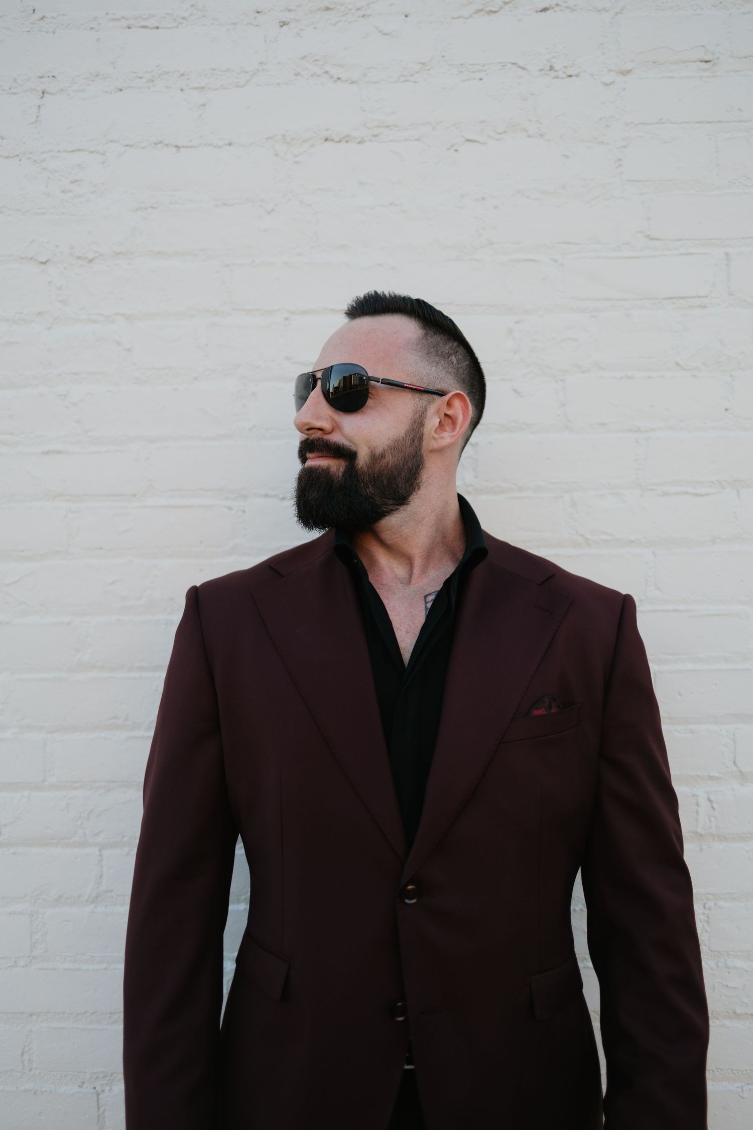 Stylish portrait series against white brick wall featuring burgundy suit jacket.