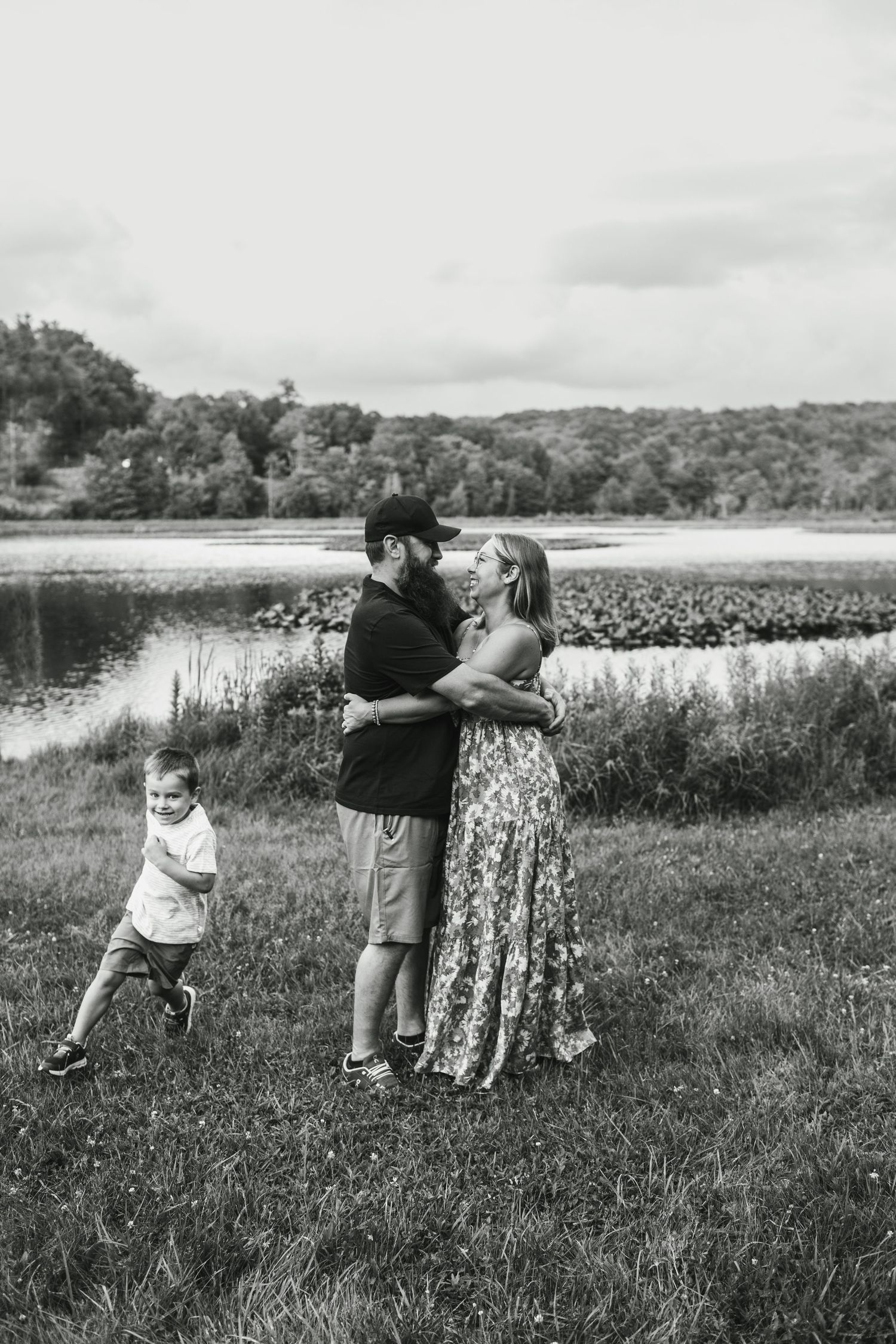 A family in white dresses sits together by a serene lake surrounded by lush forest during golden hour.