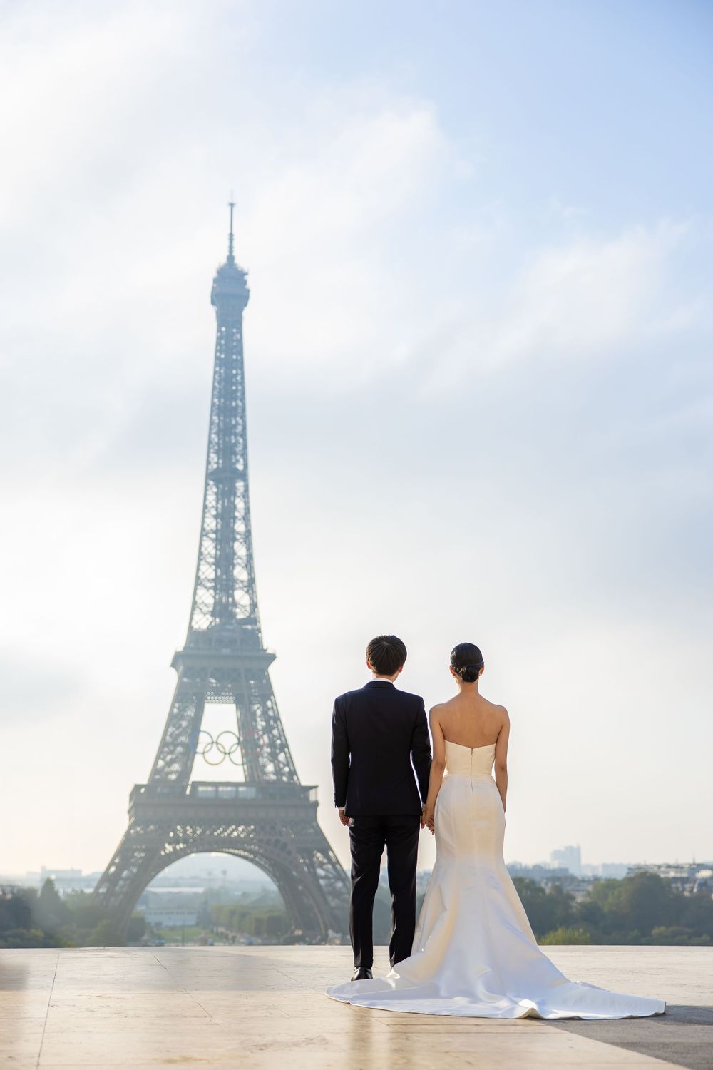 Wedding couple silhouetted against Paris skyline with Eiffel Tower panoramic composite in soft morning light.