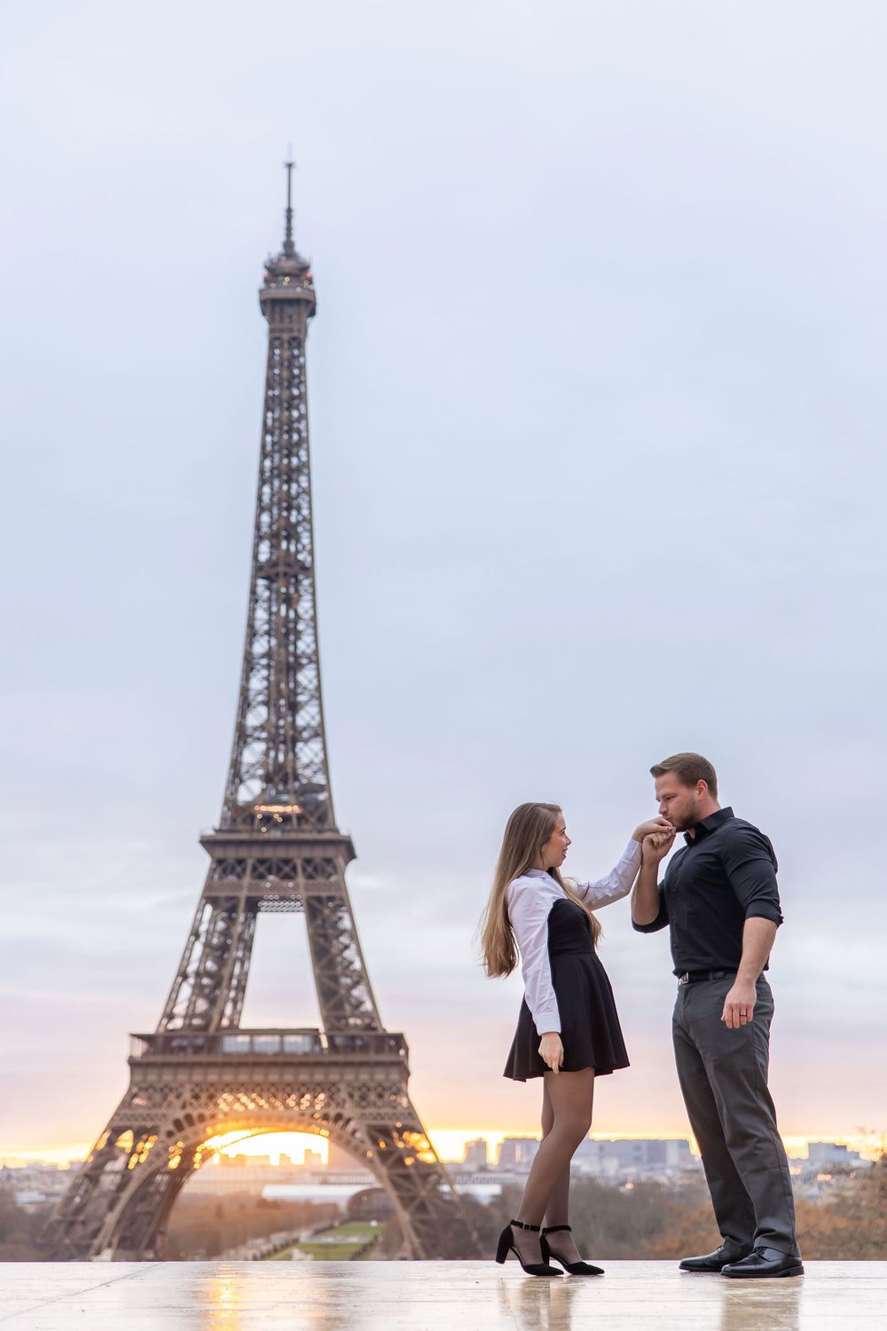 A romantic couple pose together at sunset in front of the illuminated Eiffel Tower in Paris.