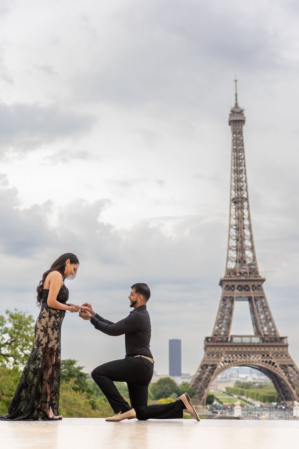 A romantic proposal scene against the backdrop of the iconic Eiffel Tower in Paris on a cloudy day.