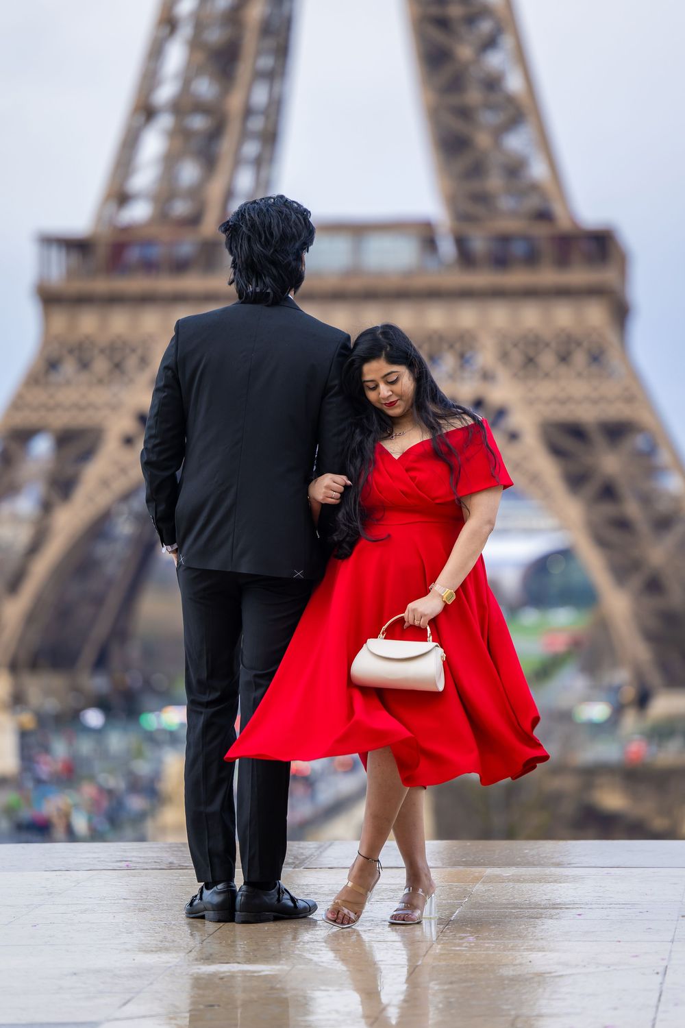 A couple stands at Trocadero square with the Eiffel Tower in background, the woman wearing a flowing red dress.