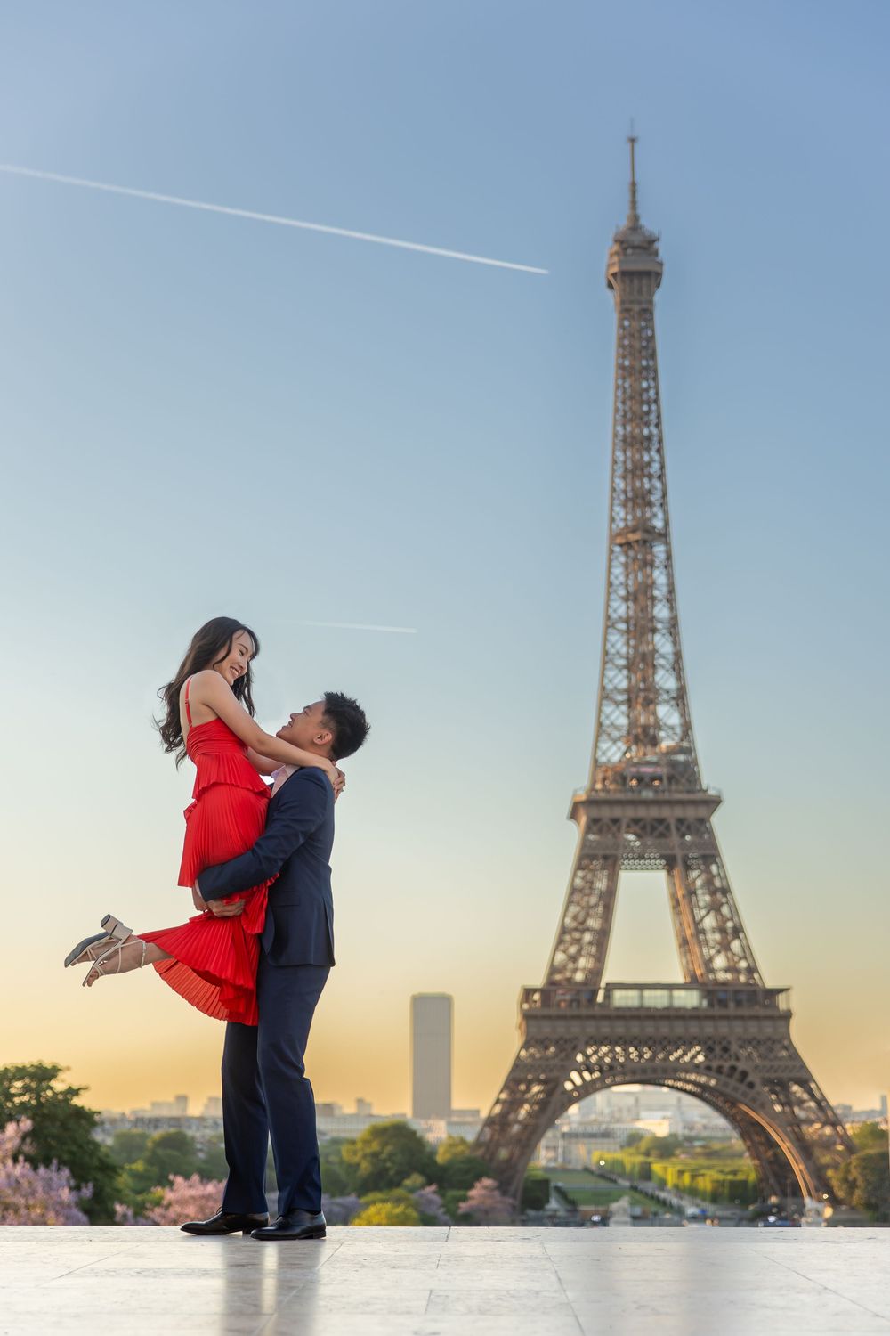 A romantic couple embraces near the Eiffel Tower in Paris during golden hour sunset, captured in a triptych photo series.