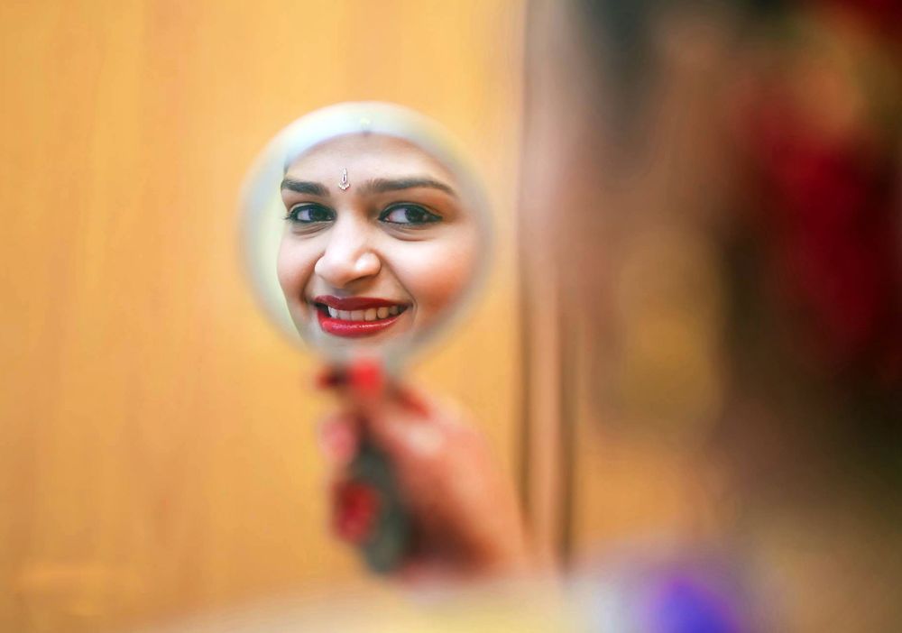 A person wearing traditional Indian bridal attire with ornate jewelry and makeup smiles in a warm-lit setting.