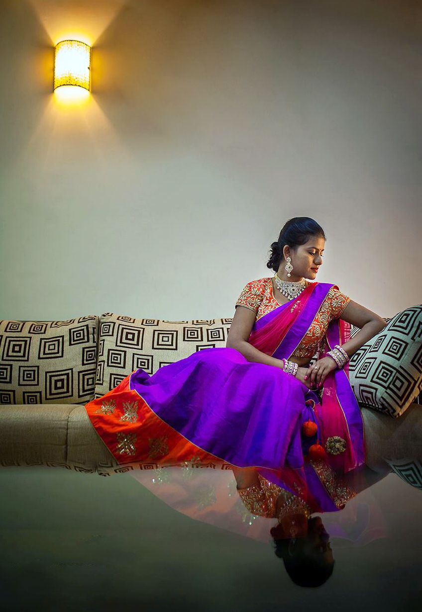 A colorful sari-clad figure reclines gracefully on a patterned couch in dramatic lighting creating an artistic portrait series.