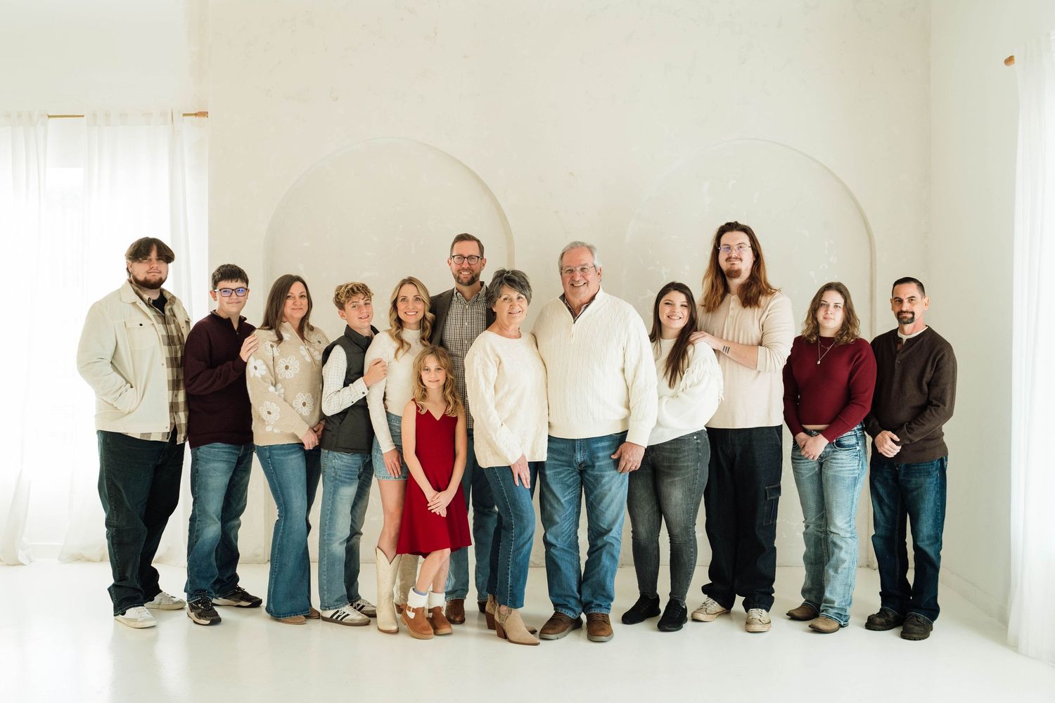 A group of people wearing casual clothing sit and stand against a white wall for a creative panoramic photo shoot.