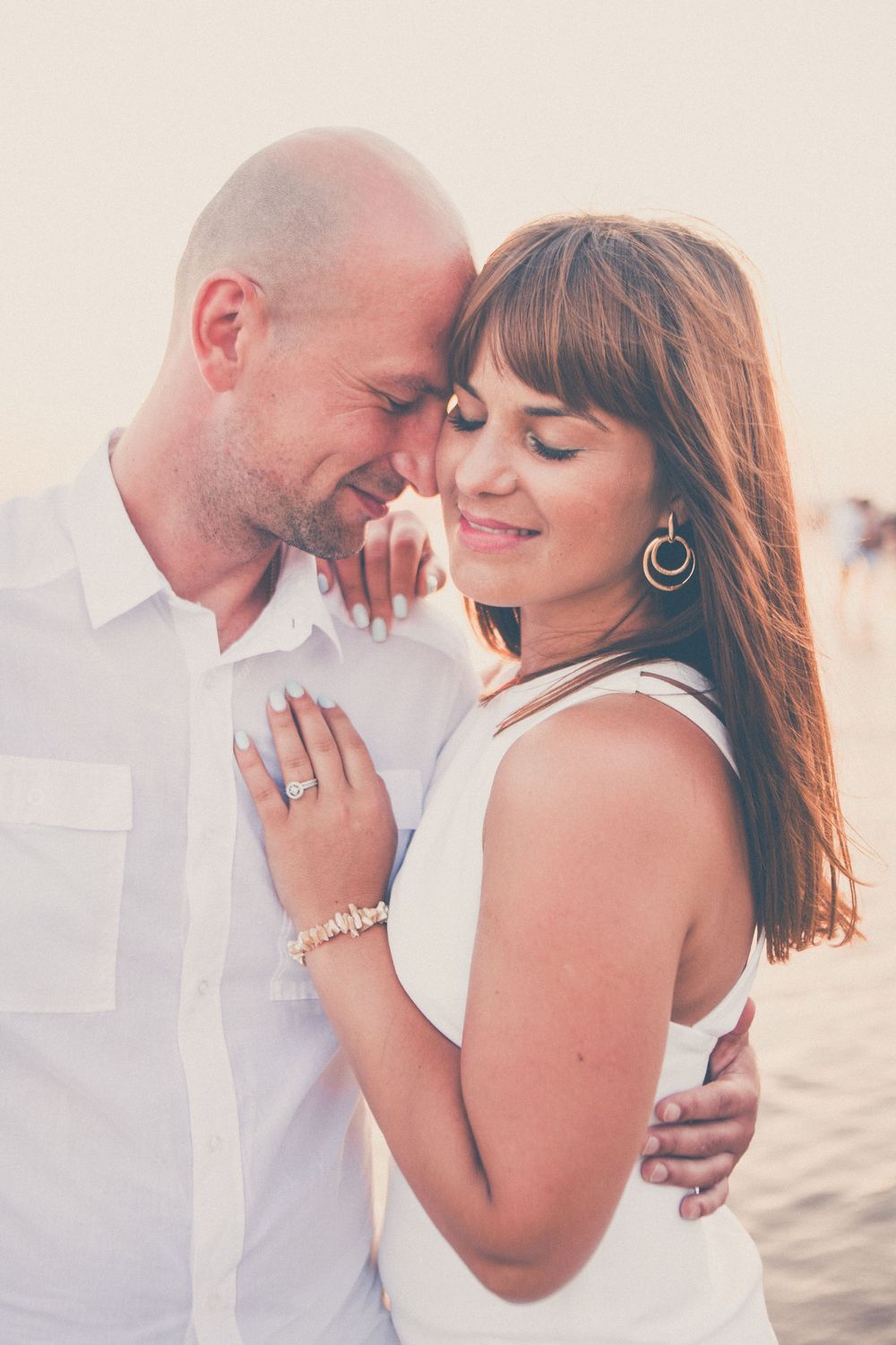 Romantic couple sharing an intimate moment in white outfits against a soft background.
