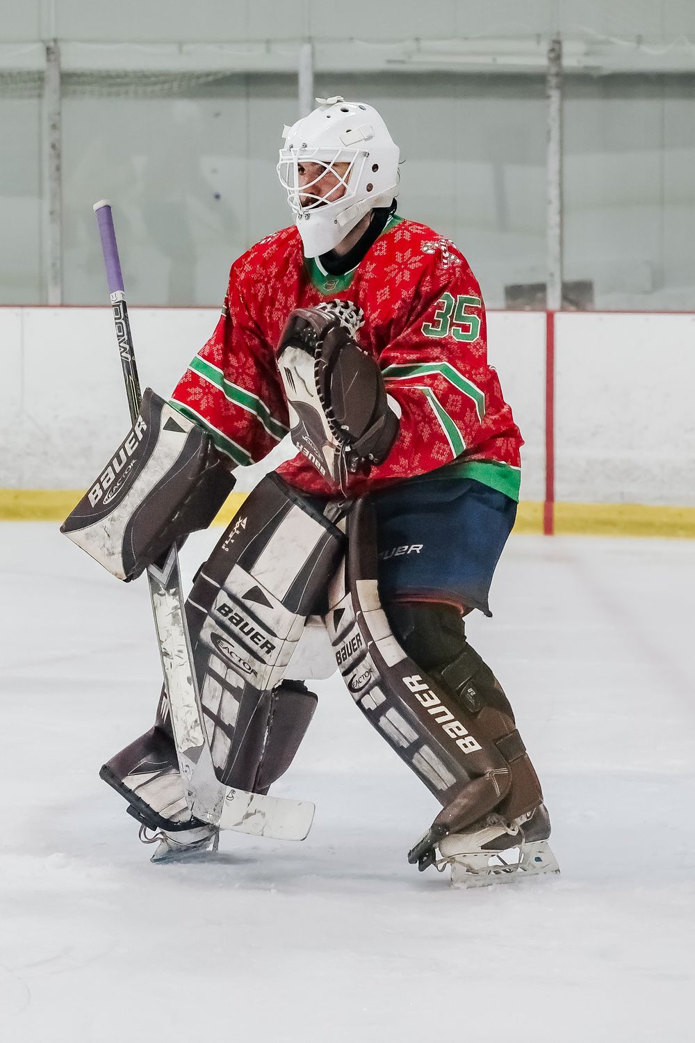 Hockey goalie in red and green jersey makes a save during an ice hockey match.