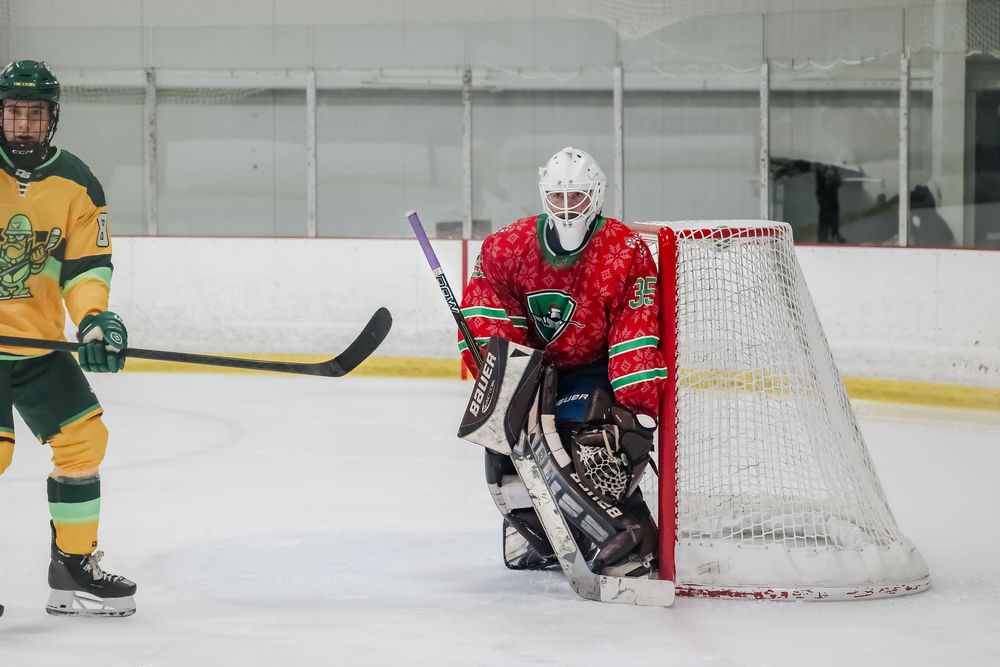 Hockey goalie defends the net while players in green and yellow jerseys approach.