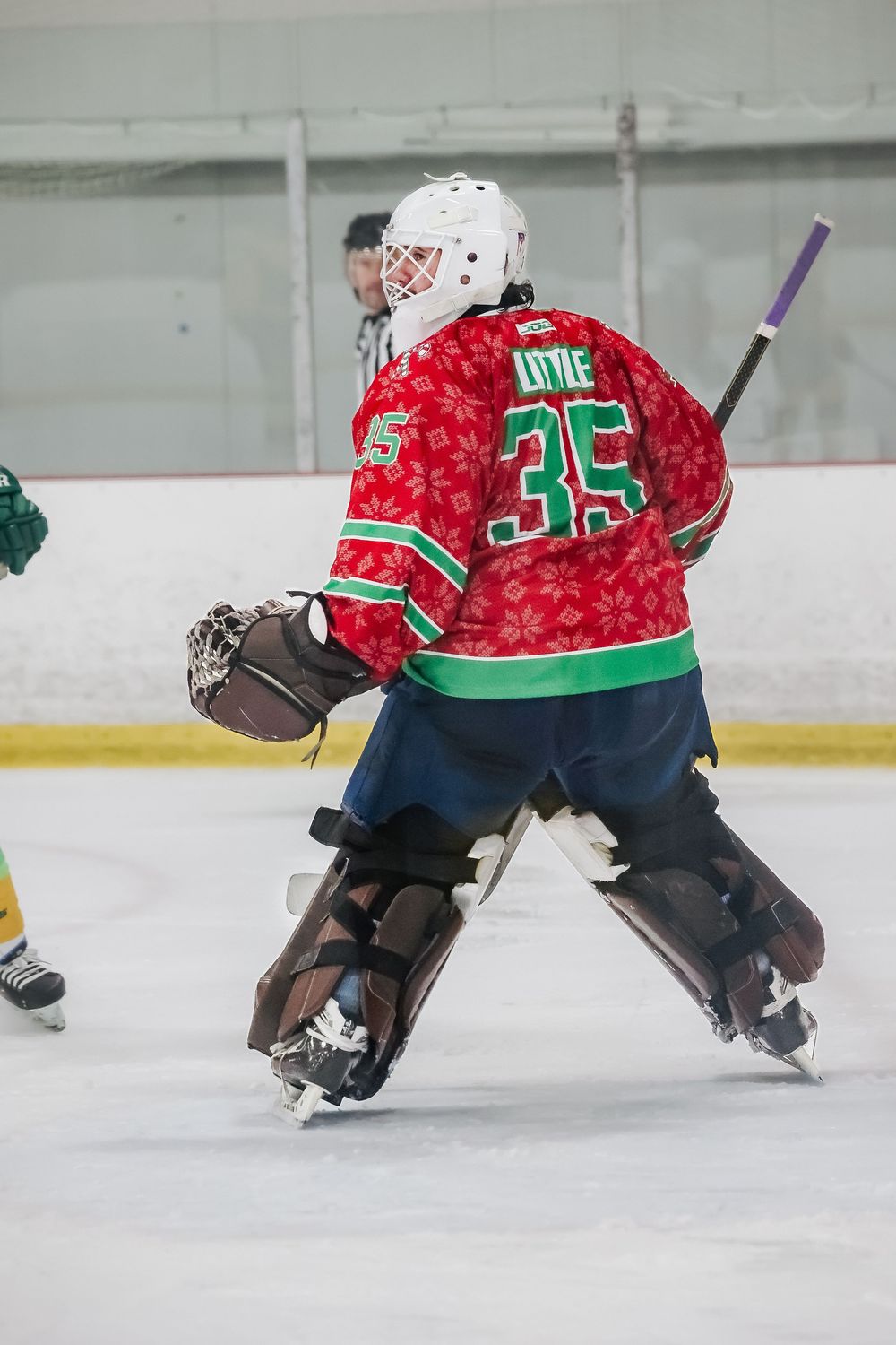 Hockey goalie in festive red jersey slides across ice to make save.