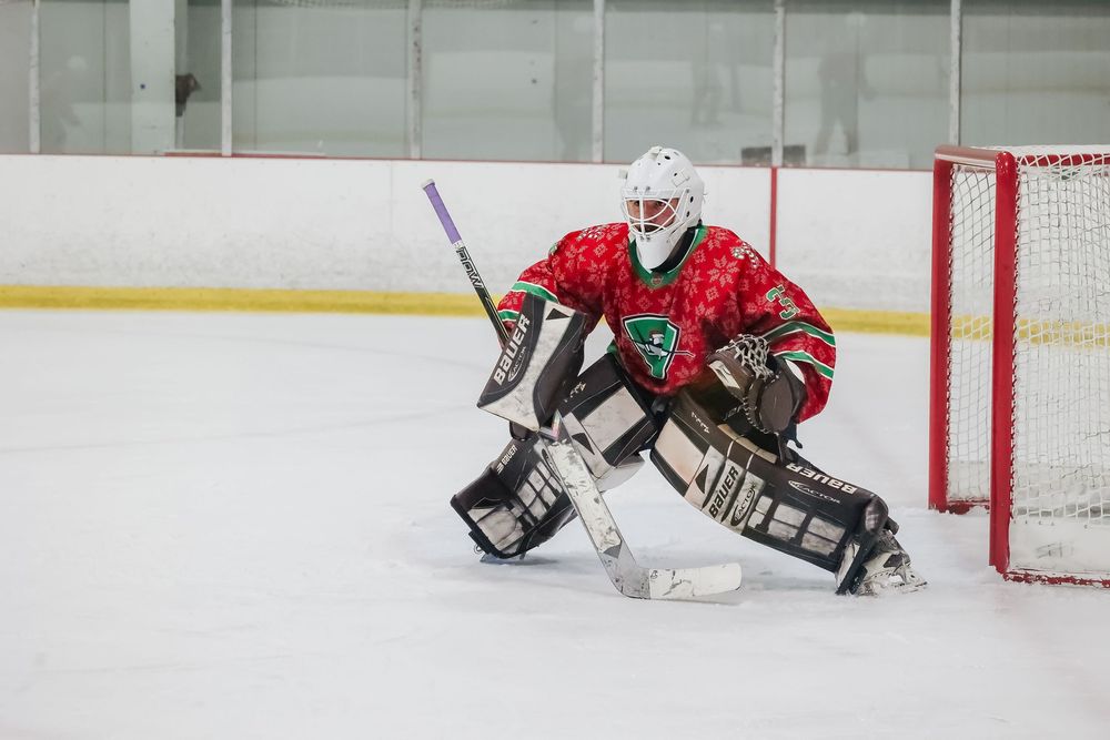 Hockey goalie in red and green jersey makes a save during an ice hockey game.
