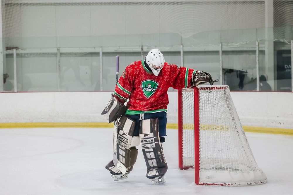 Ice hockey goalie in festive red jersey defends the net during practice.