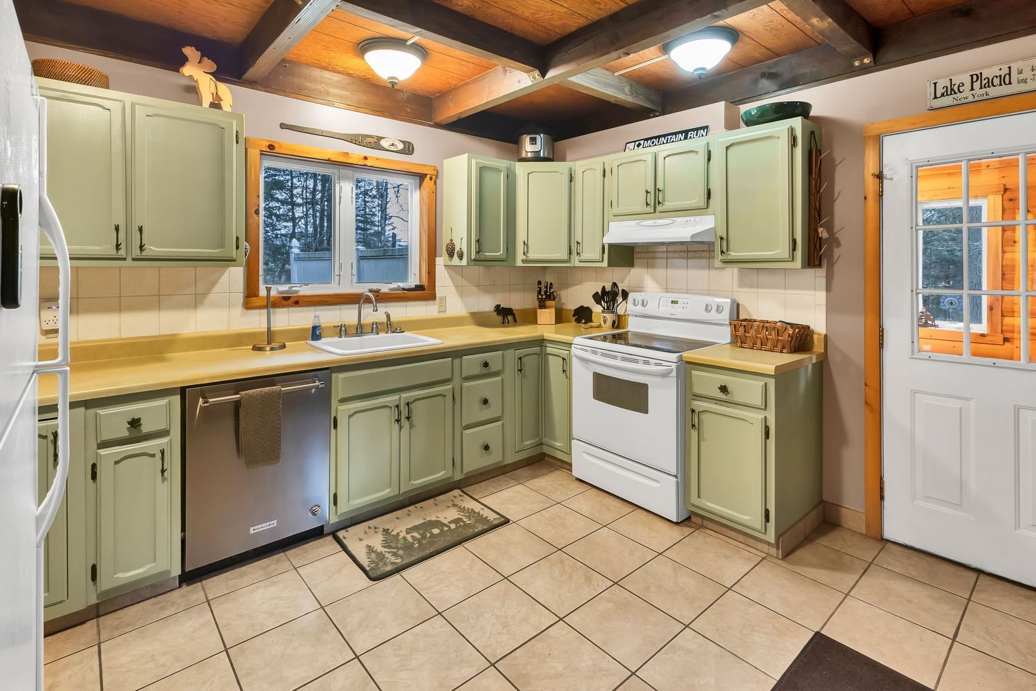 Spacious kitchen with sage green cabinets, exposed wood beams, and tile flooring features modern appliances and ample storage.