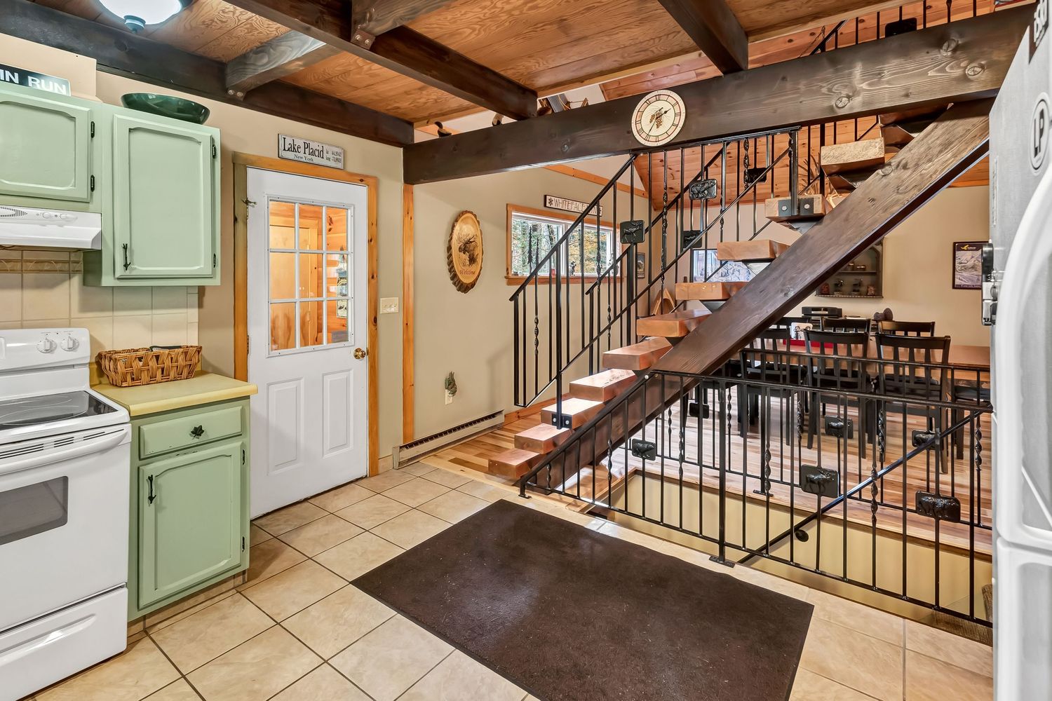 Rustic kitchen interior with mint green cabinets, wooden beams, and wrought iron staircase leading upstairs.