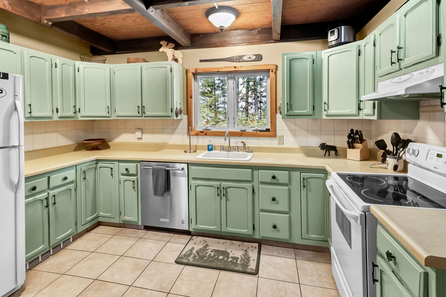 Spacious mint green kitchen with white countertops, wood beam ceiling, and pendant lighting showcases traditional cabinetry.