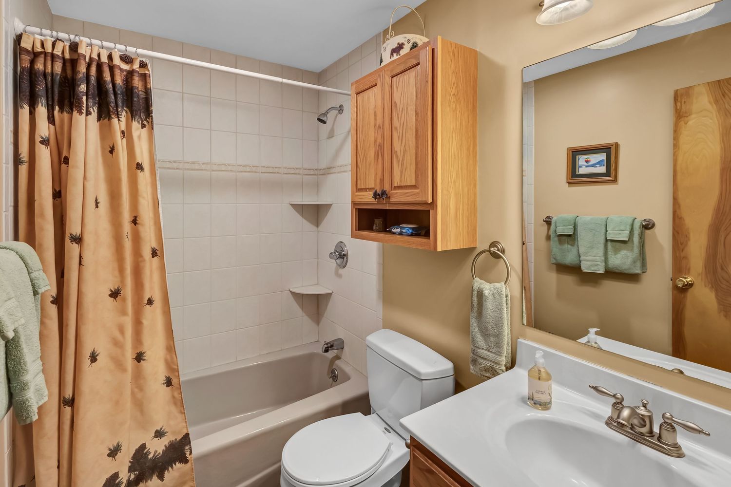 Cozy bathroom interior with oak cabinets, polka dot shower curtain, and mint green towels on display.