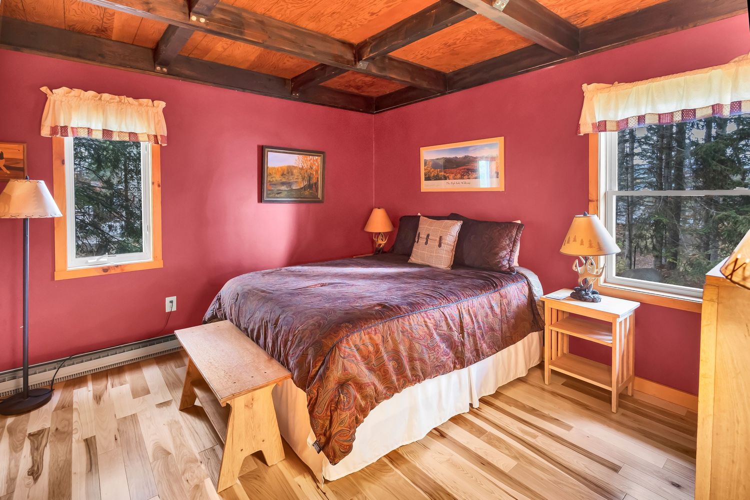 Cozy bedroom with red walls, hardwood floors, and exposed wooden beams features a king bed and rustic decor.