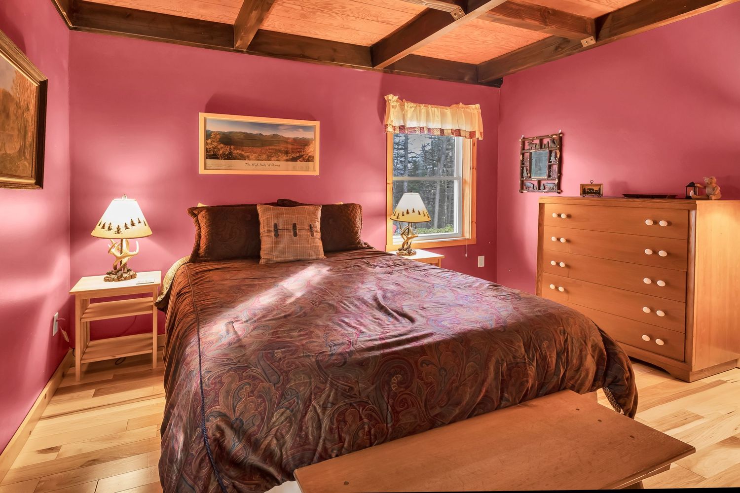 Cozy bedroom with pink walls, wooden furniture, exposed ceiling beams, and a brown comforter on the bed.