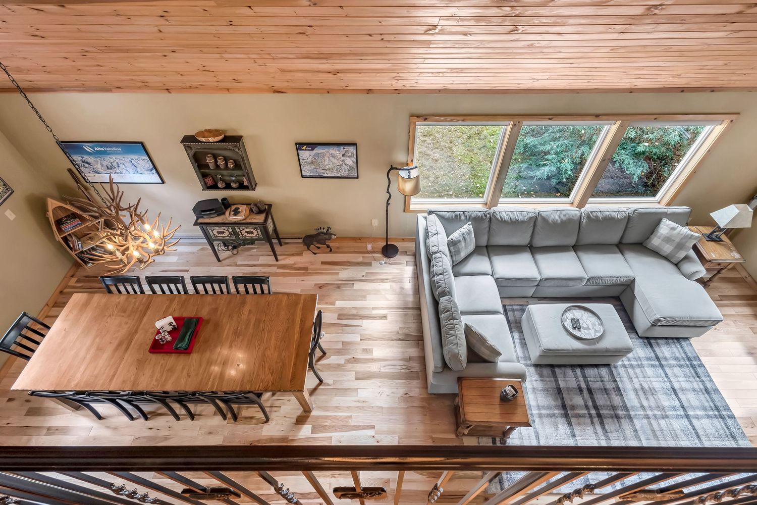 Modern open-concept living area with grey sectional sofa, wooden dining table, and vaulted ceiling with skylights.