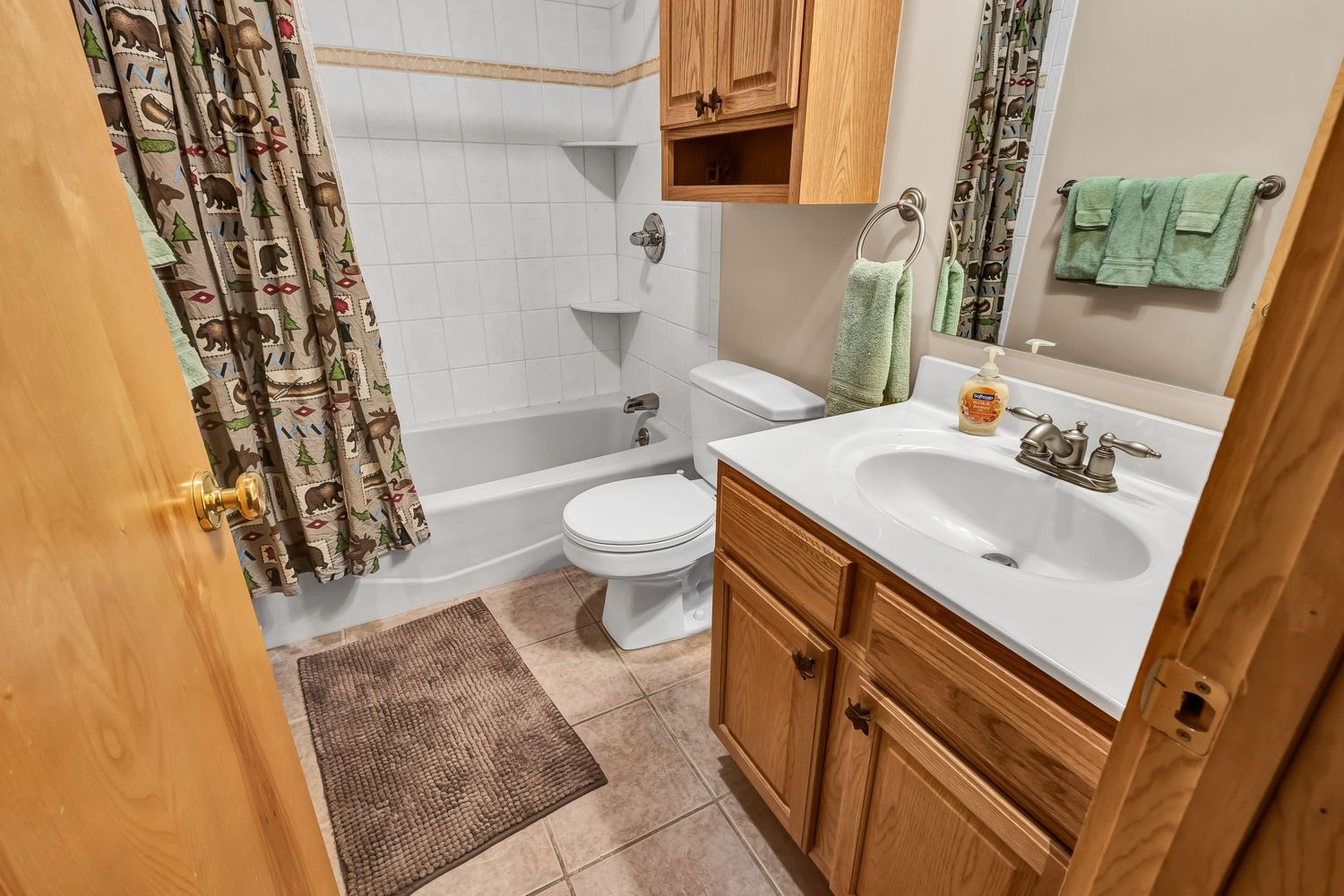 Clean bathroom with wooden cabinets, white countertop, floral shower curtain, and brown bath mat.